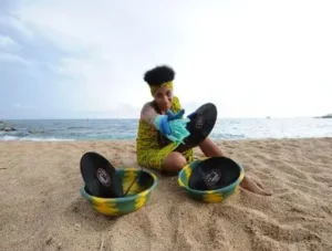 djatodocolor en la playa, lavando vinilos con cubos coloridos, fusionando música y naturaleza en una escena única.