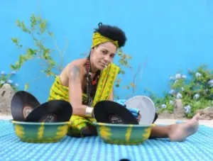 djatodocolor lavando Discos de vinilo con atuendo amarillo y verde, usando guantes azules, rodeada de plantas y flores.