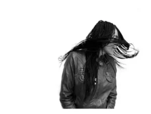 Retrato en blanco y negro de mujer con trenzas al viento, vistiendo chaqueta de cuero y mirando hacia la derecha.