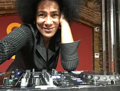 Fotografia-djatodocolor-Directo-By-SalaGatzara djatodocolor posando sonriente junto a su equipo de mezcla, preparada para ofrecer una experiencia musical en un espacio cerrado con estilo.